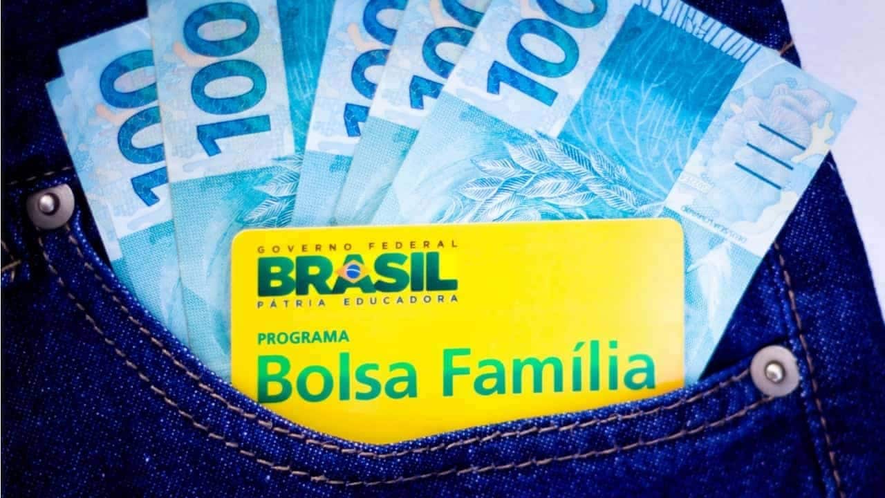 Cartão do Bolsa Família e notas de 100 reais no bolso de uma roupa jeans