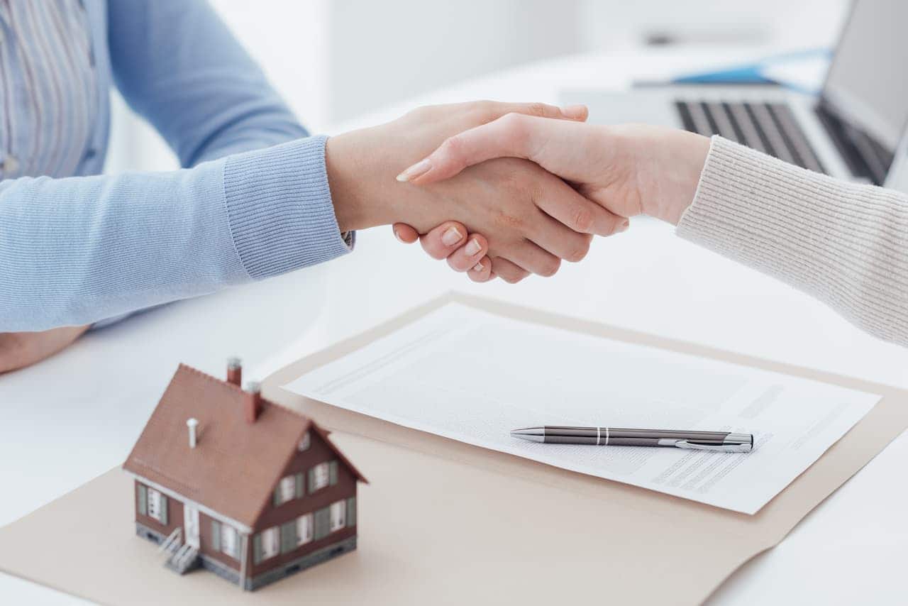Mesa com um ícone de uma casa e aperto de mãos simbolizando um contrato entre cliente e agente