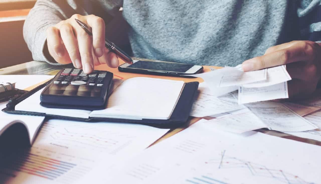 Imagem de uma pessoa calculando e analisando diversos documentos.