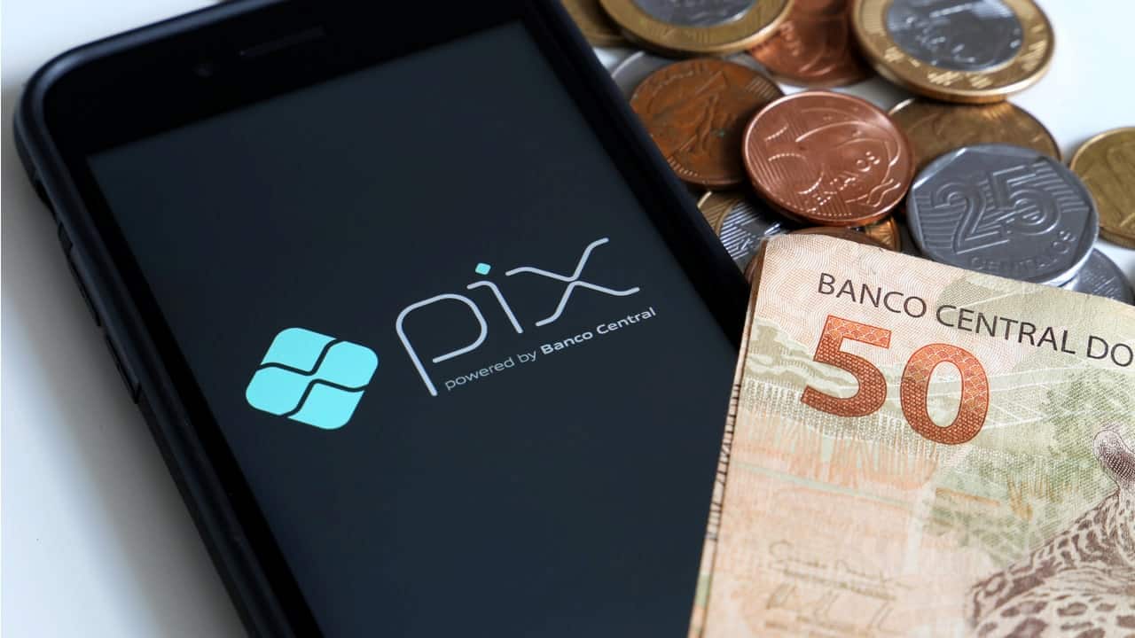 celular com tela inicial do Pix ao lado de várias moedas e nota de 50 reais