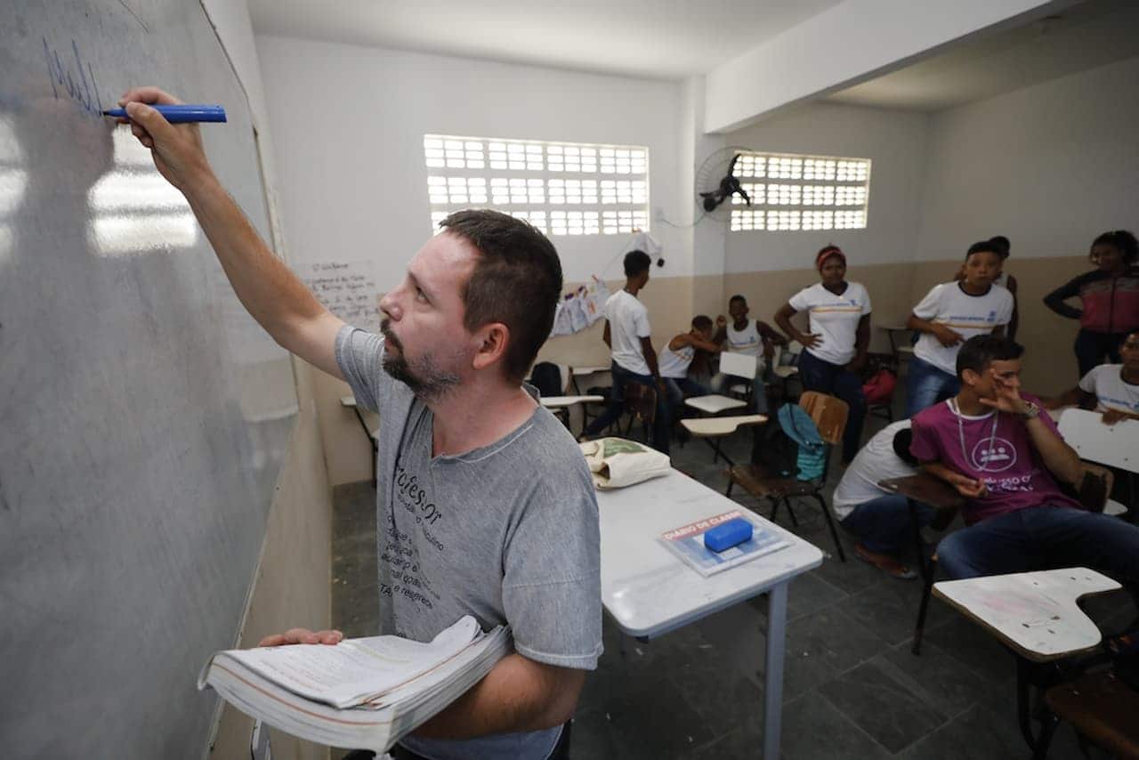 Professor escrevendo na lousa para alunos em uma sala de aula com bolsa por frequência escolar