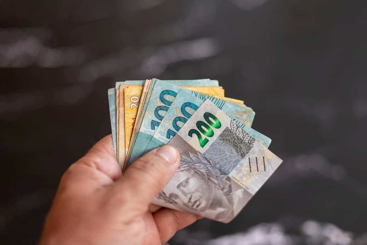 Uma mão segurando um "bolo" de notas de 200 e 100 reais