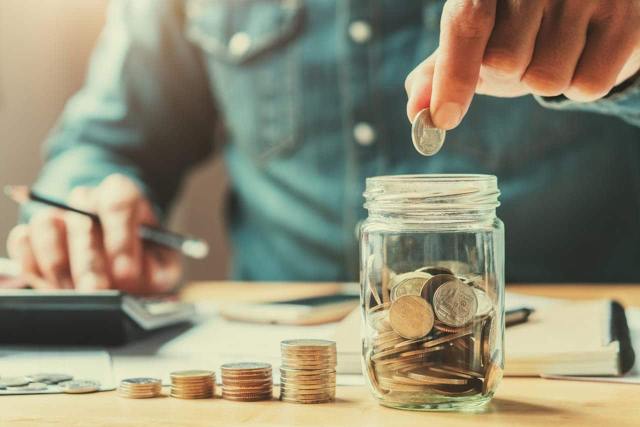Homem colocando moedas em um pote enquanto utiliza uma calculadora