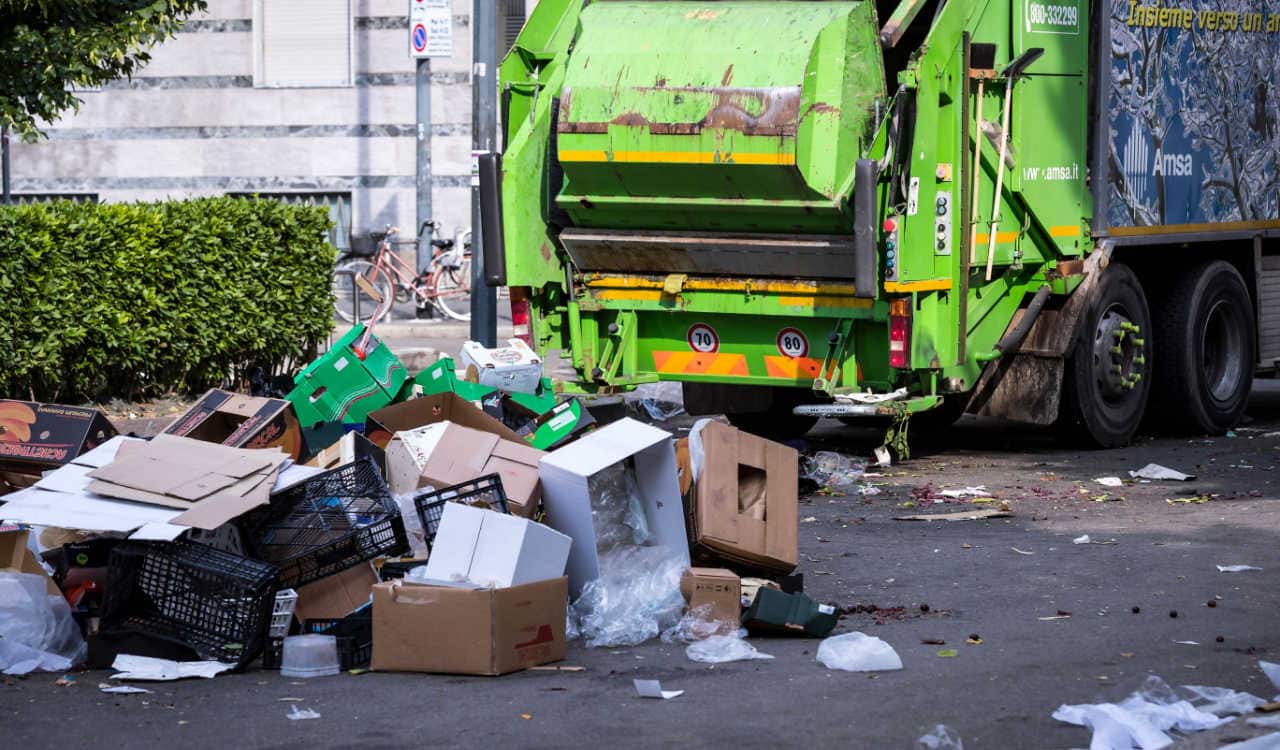 Uma pilha de lixo na rua e um caminhão de coleta parado ao fundo
