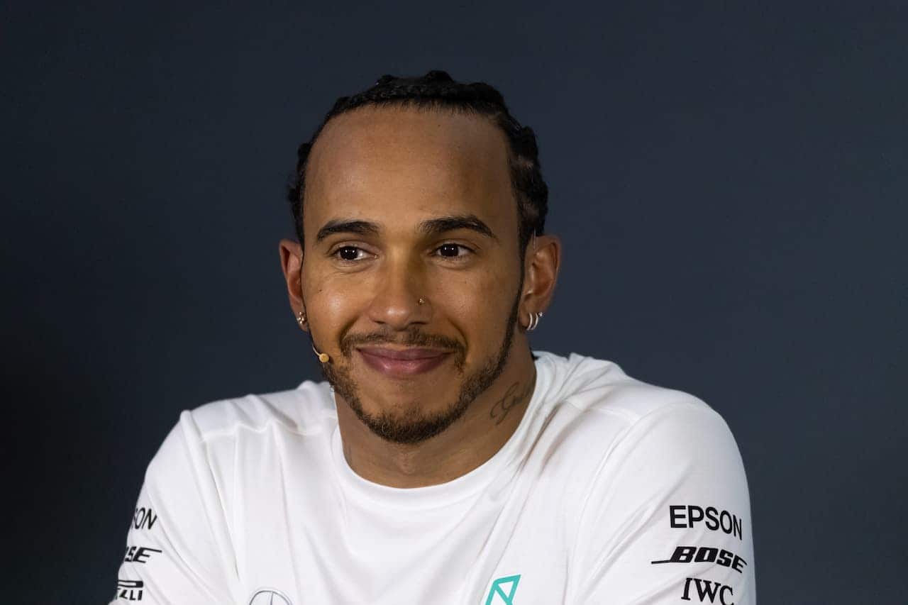 Lewis Hamilton de camisa branca em um fundo azul escuro hamburgueria