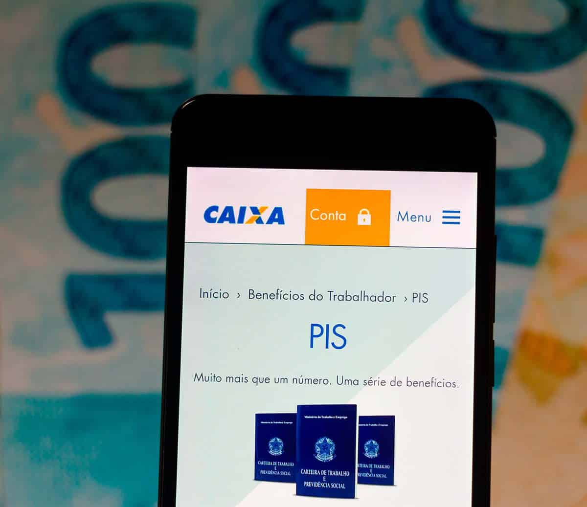 Celular aberto no site da Caixa, na página do PIS, e notas de dinheiro atrás