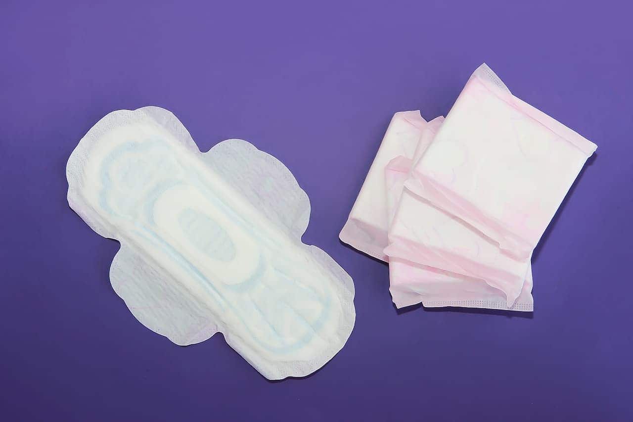um absorvente aberto e três absorventes fechados sobre uma superfície lisa e roxa