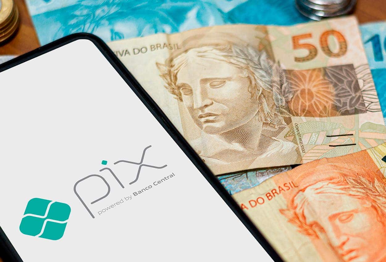 imagem de um celular exibindo página do app Pix, ao lado de notas de dinheiro e moedas