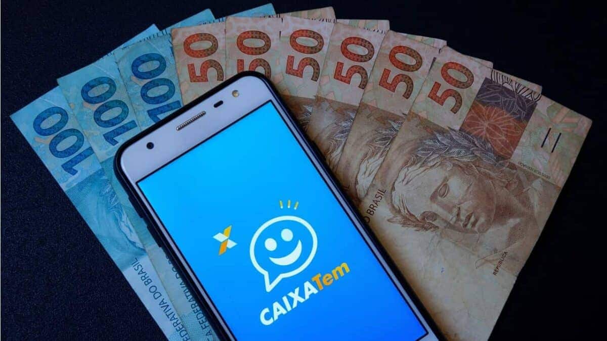 Celular com o app do Caixa Tem aberto sobre notas de 100 e 50 reais