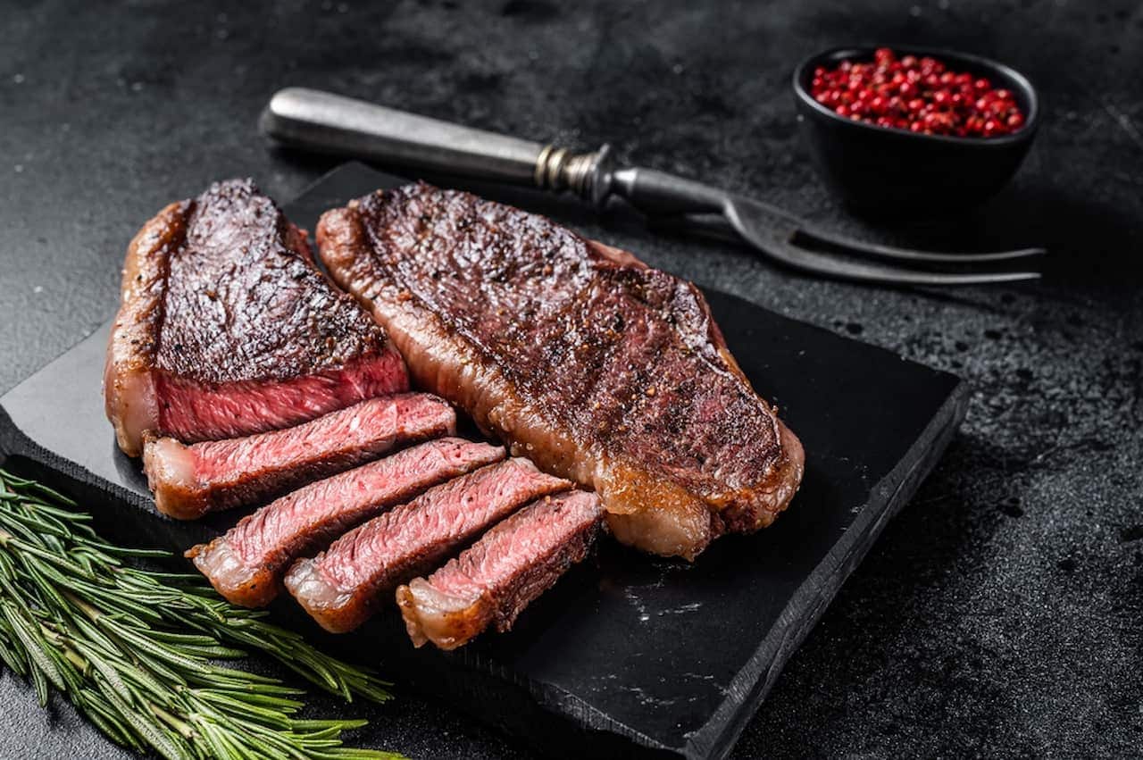 Carne fatiada sobre granito, ao lado de um garfo e temperos