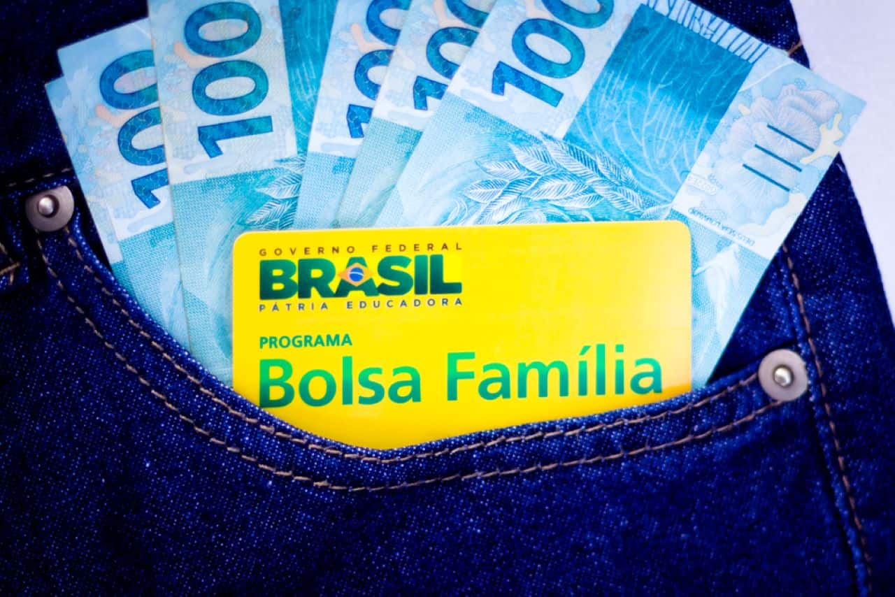 Cartão do bolsa família e notas de cem reais em um bolso de calça jeans