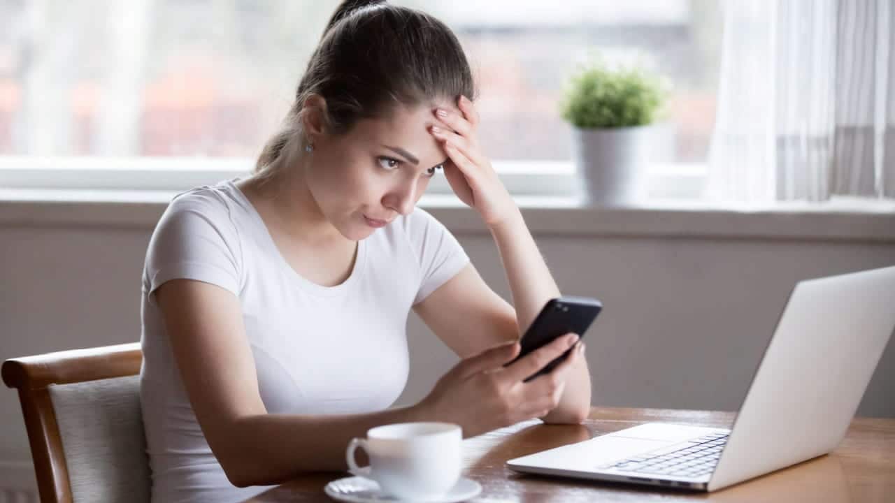 cliente de banco chateada olha para noticia no celular com olhar de desaprovação