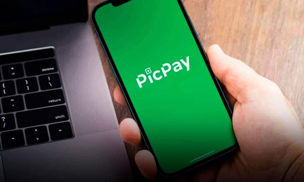 Celular com PicPay aberto e notebook ao fundo sobre uma superfície marrom