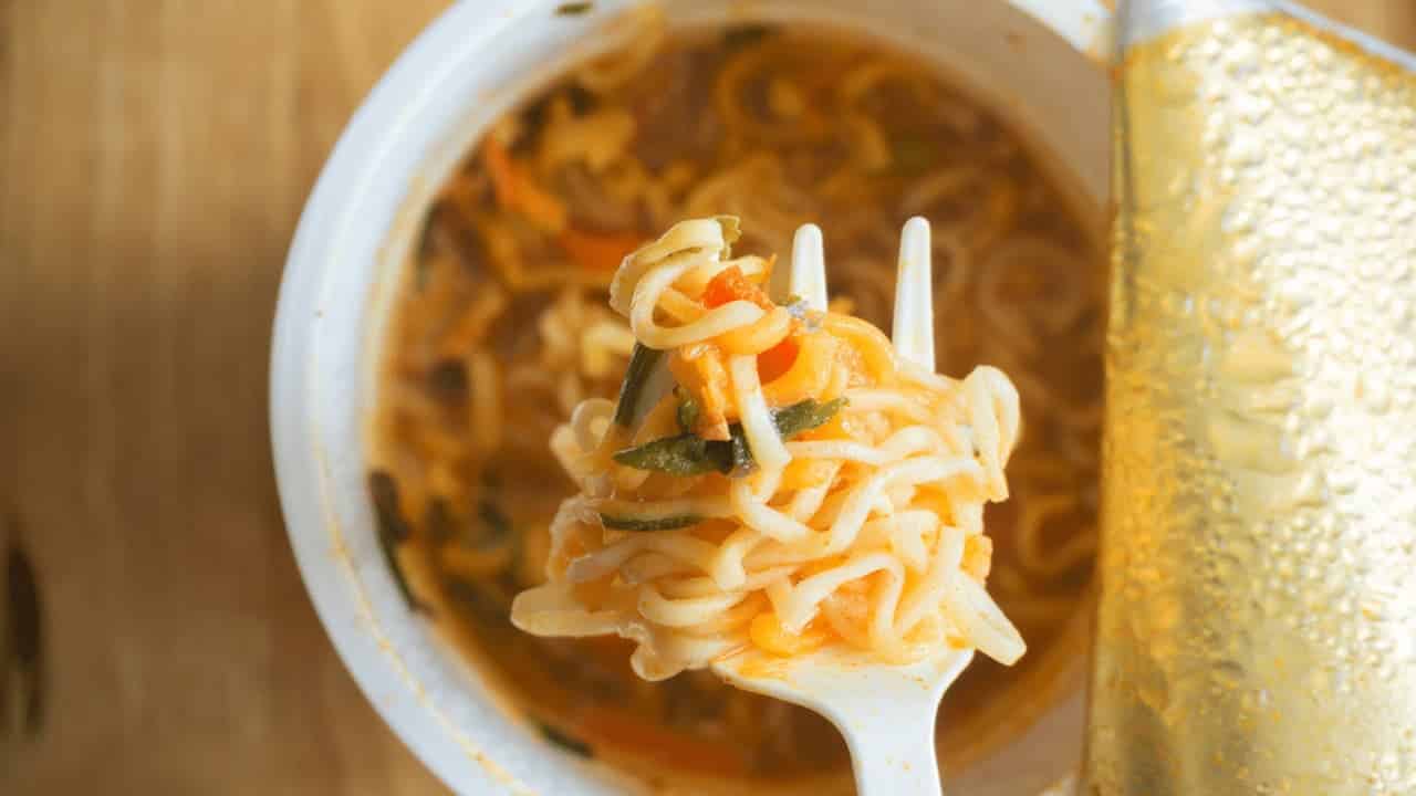 Garfo segurando um pouco de macarrão, pote de cup noodles aberto embaixo
