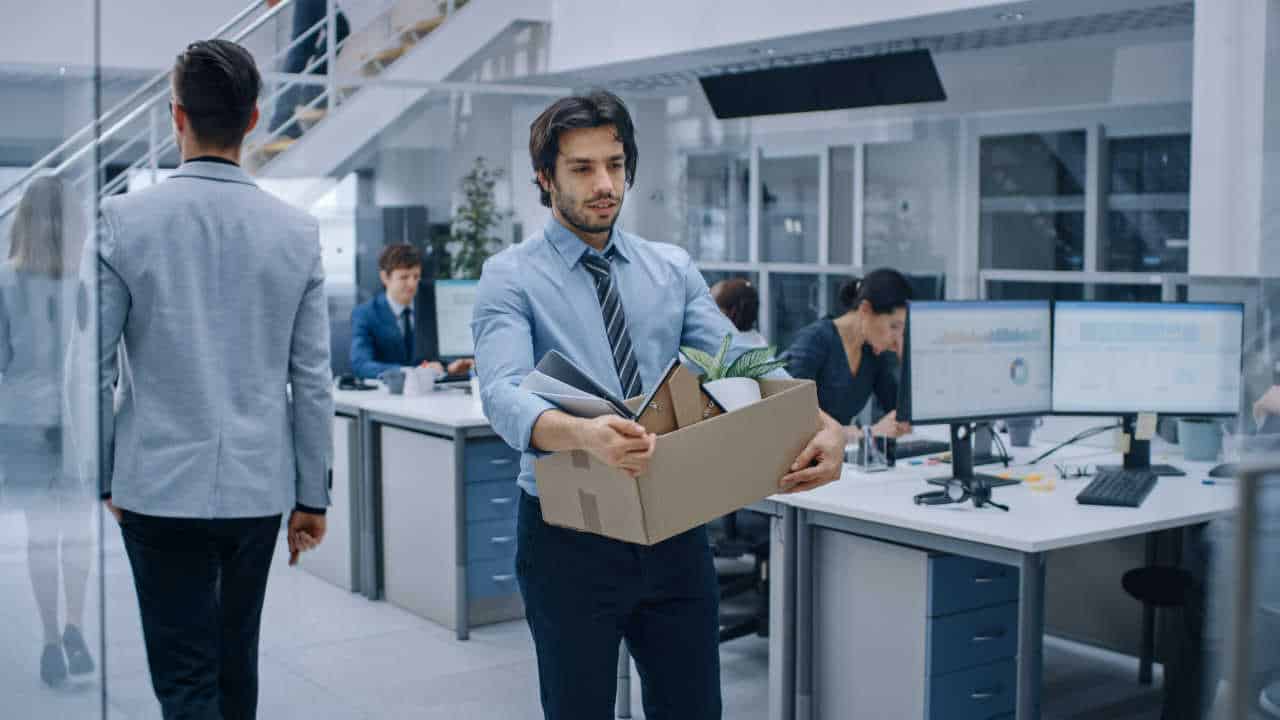 funcionário saindo da empresa segurando uma caixa com os seus pertences