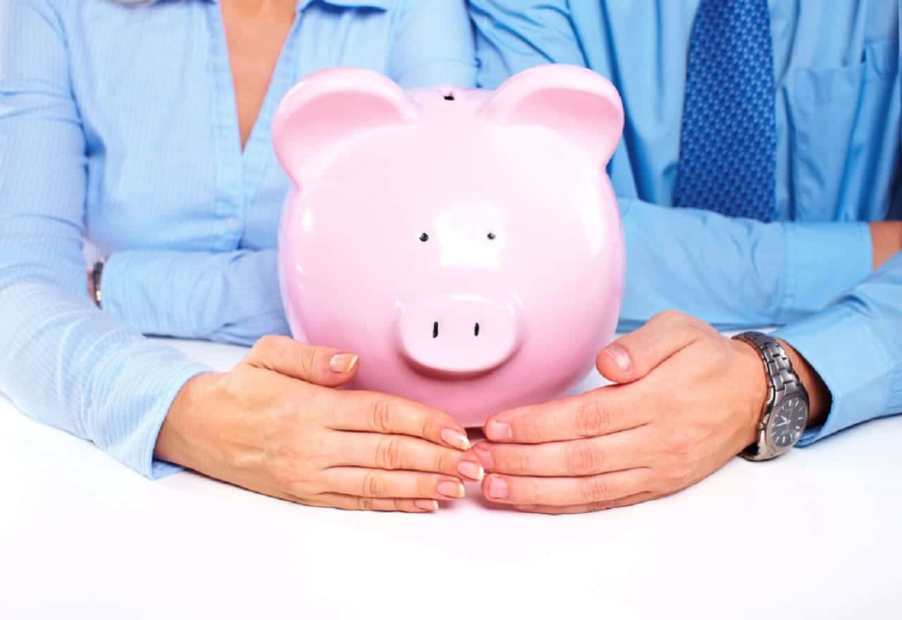 Imagem de uma mulher e um homem, ambos de camisa azul. À frente deles, um cofrinho em formato de porquinho. Ambos colocam uma mão na frente do cofrinho.