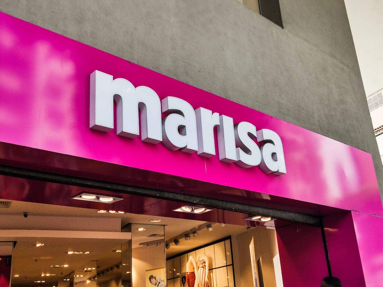 Sobre fundo cinza de um prédio, logo de uma loja Marisa