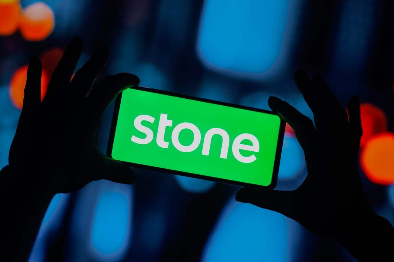 mãos segurando celular com logo da Stone