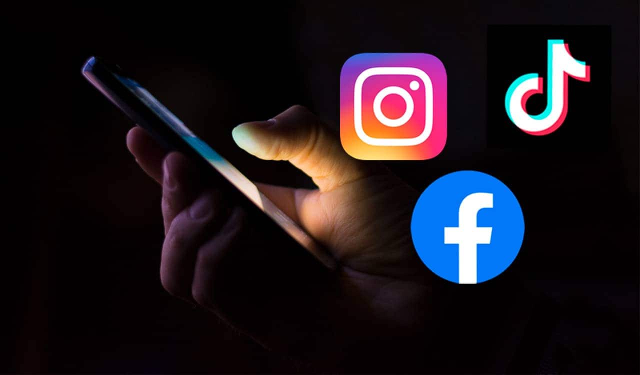 Mão segurando um celular ao lado dos aplicativos Instagram, Facebook e TikTok promoções falsas
