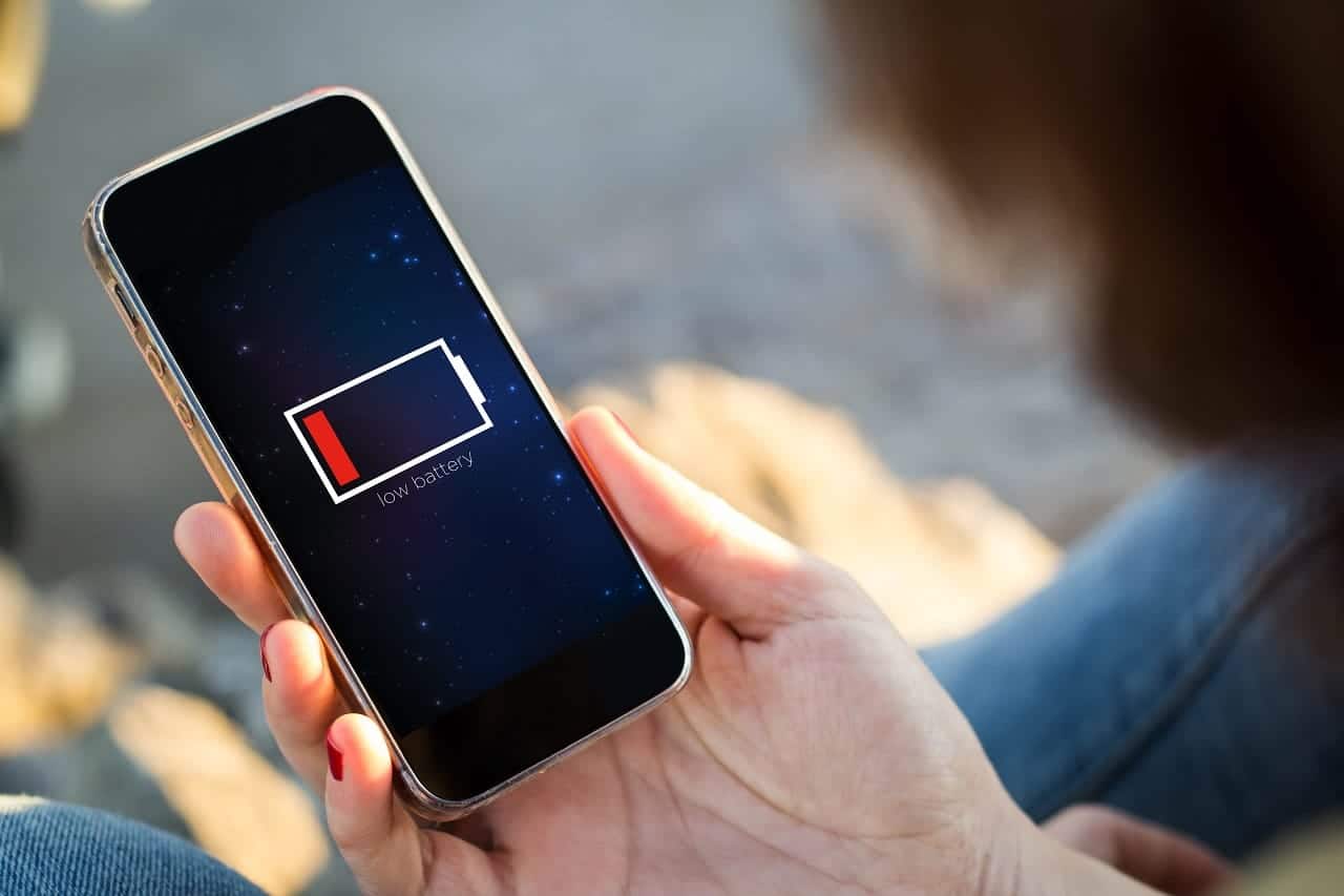 Uma mão segurando um celular visto de cima. A tela do aparelho está preta e no meio aparece o sinal de bateria vazia. IOS 19