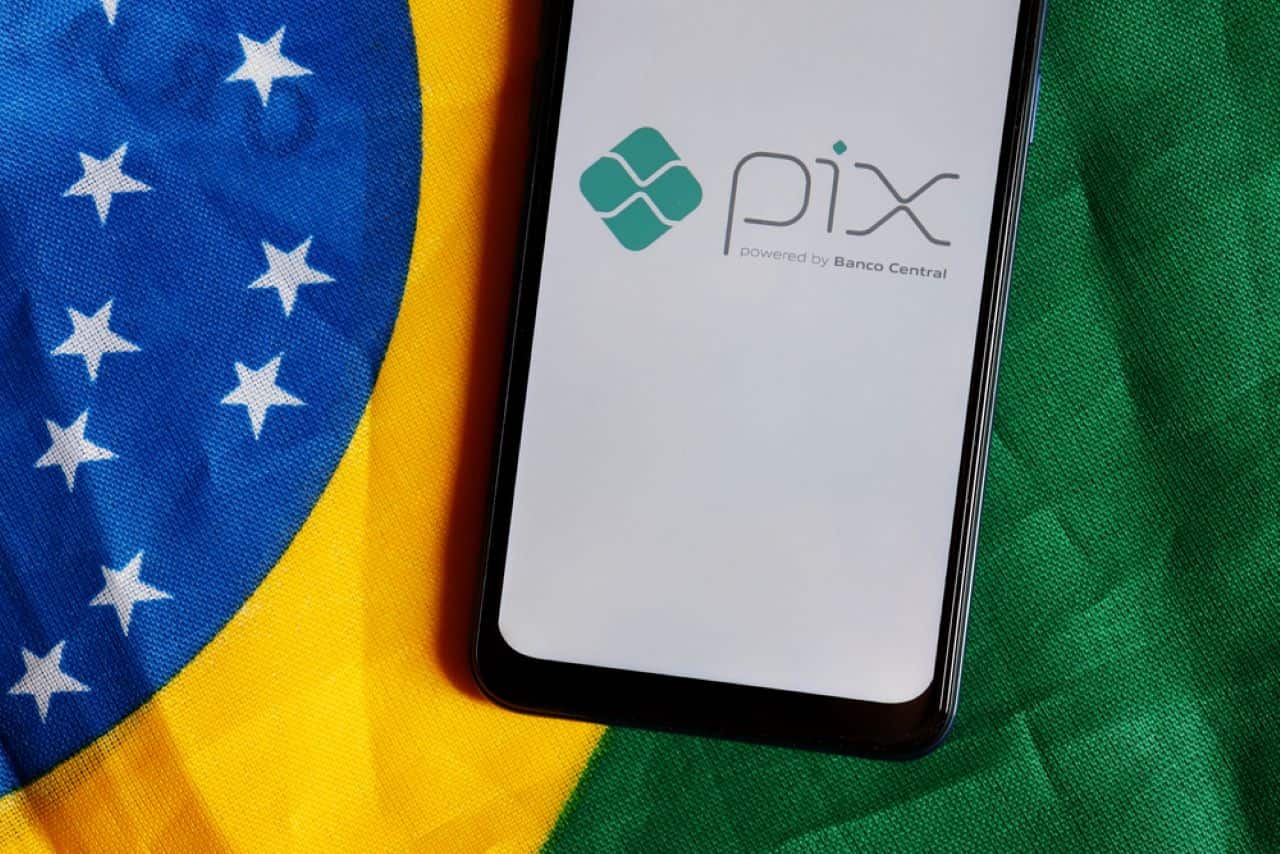 celular exibindo a logo do Pix na tela com a bandeira do Brasil no fundo