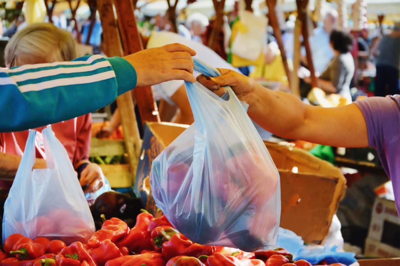 sacola de plástico com verduras sendo recebida por uma pessoa dentro do supermercado