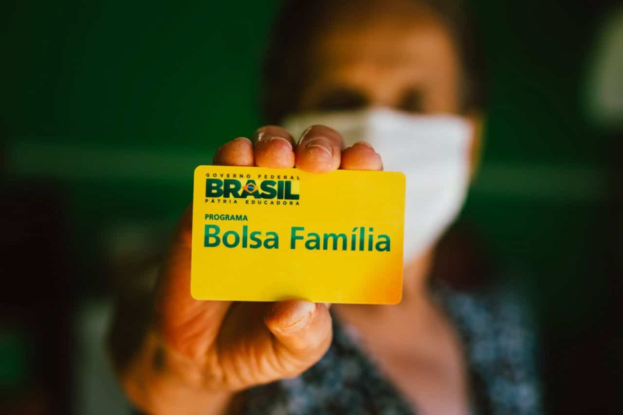 senhora com o rosto desfocado segurando um cartão do bolsa família