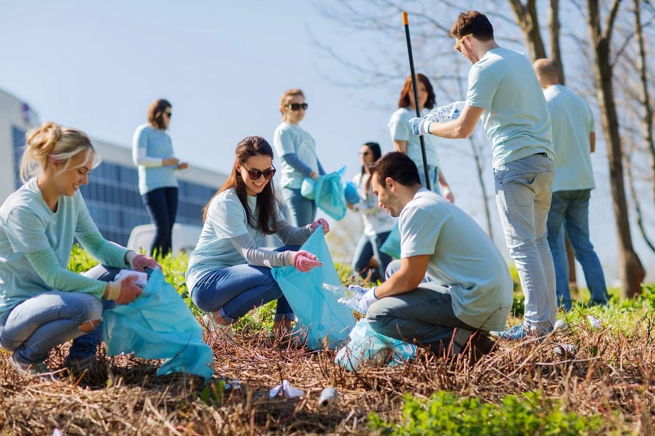 Imagem mostra voluntários vestidos de camisas na cor azul claro enquanto recolhem lixo em um terreno.
