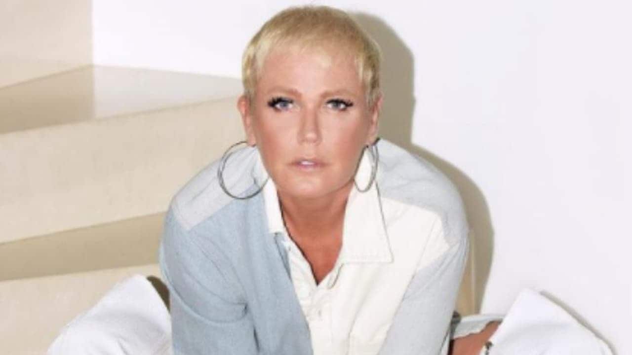 Xuxa vestindo uma blusa branca com brincos dourados em frente a fundo branco