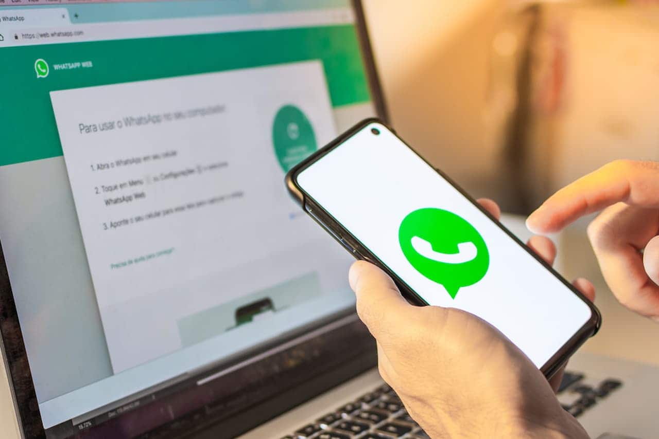 Celular com WhatsApp aberto e notebook ao fundo