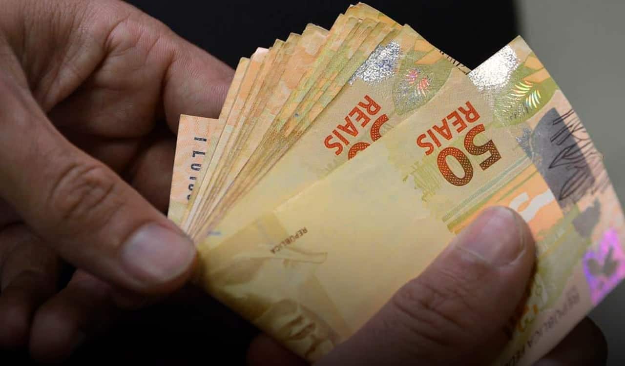 Mão segurando várias notas de cinquenta reais Empréstimo consignado