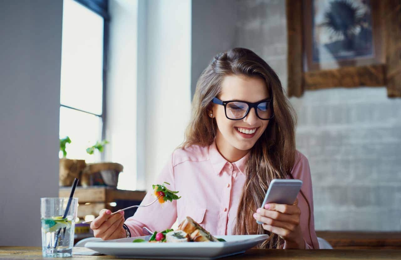 Mulher comendo em restaurante e pagando com cartão de crédito