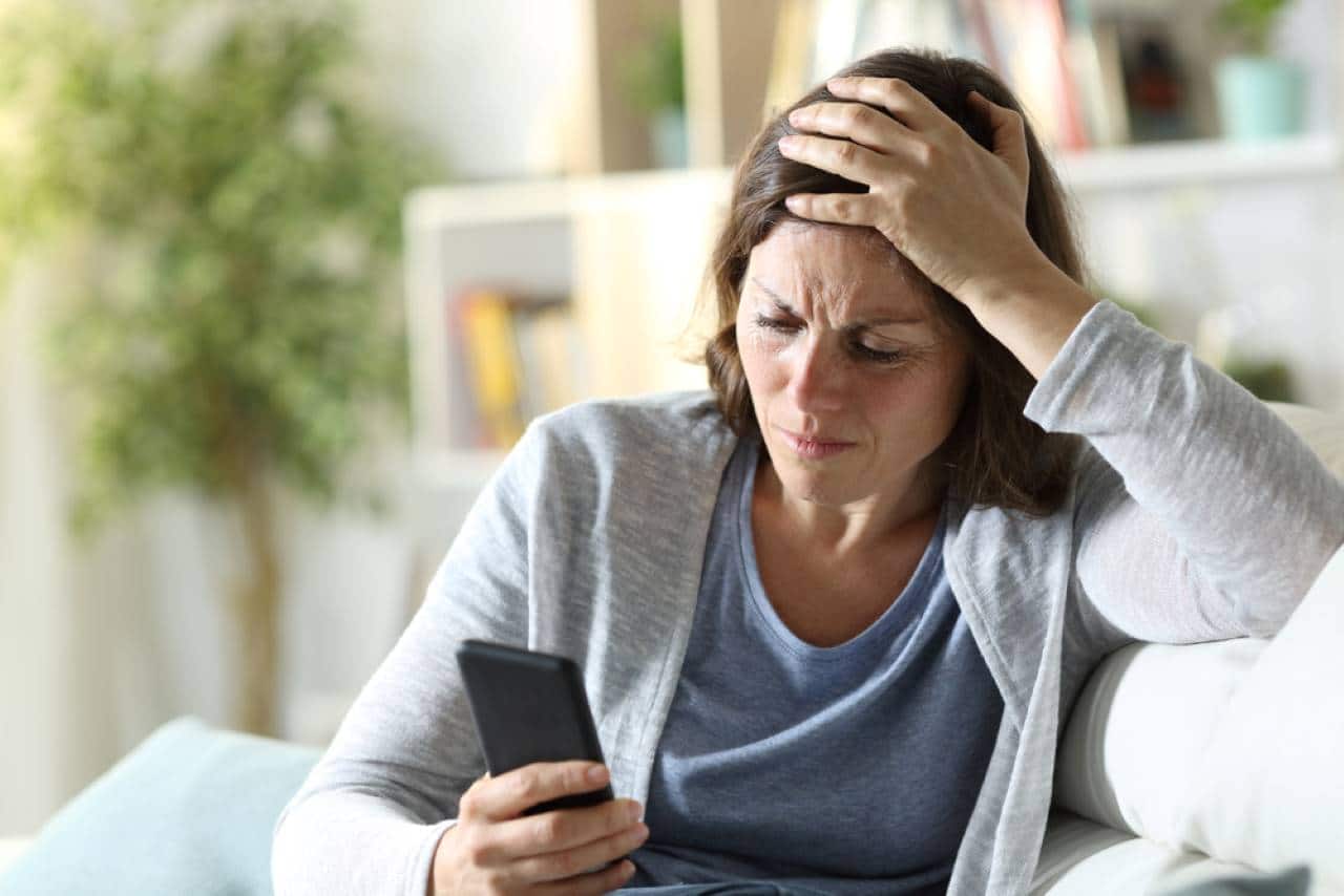 mulher com expressão preocupada, olhando o celular.