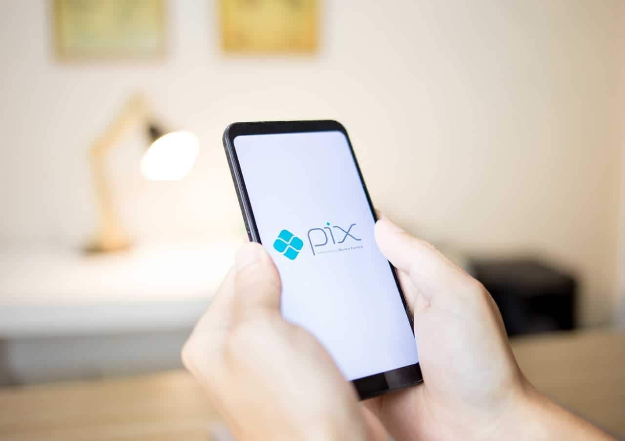 Duas mãos segurando um celular com a tela na logo do PIX