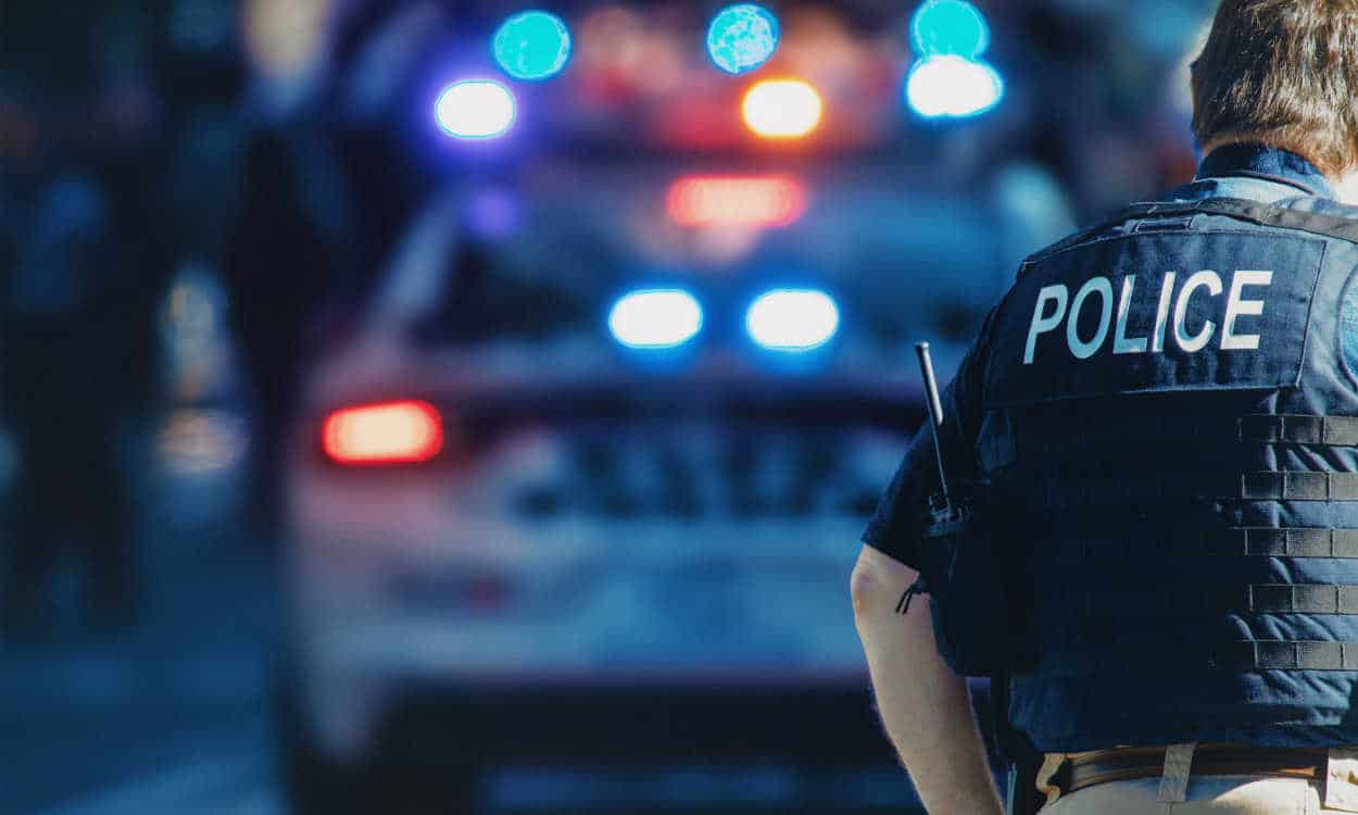 Agente da polícia americana de costas com uma viatura ao fundo