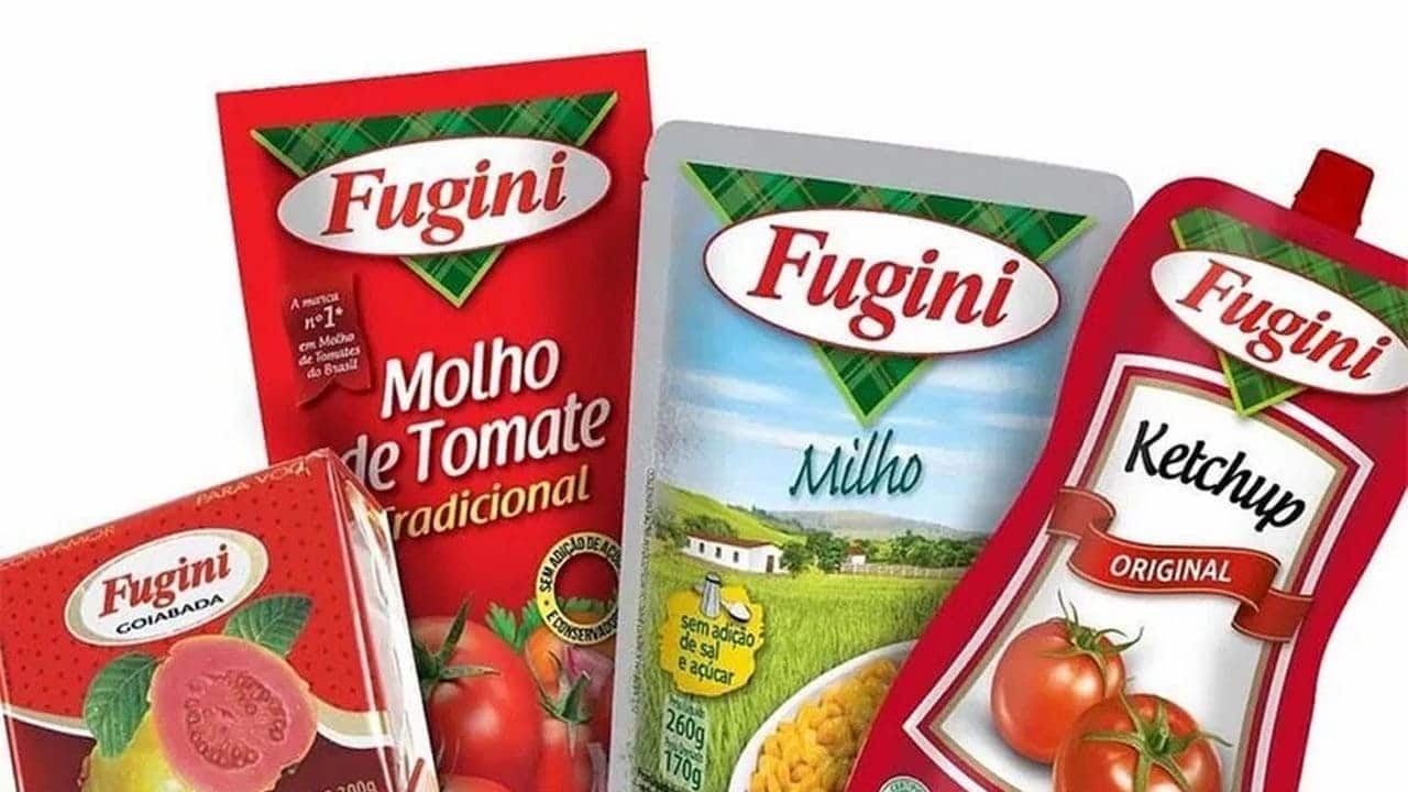 Na imagem, diante de um fundo branco, está um grupo de alimentos da marca Fugini, como molho de tomate, milho, goiabada e ketchup.
