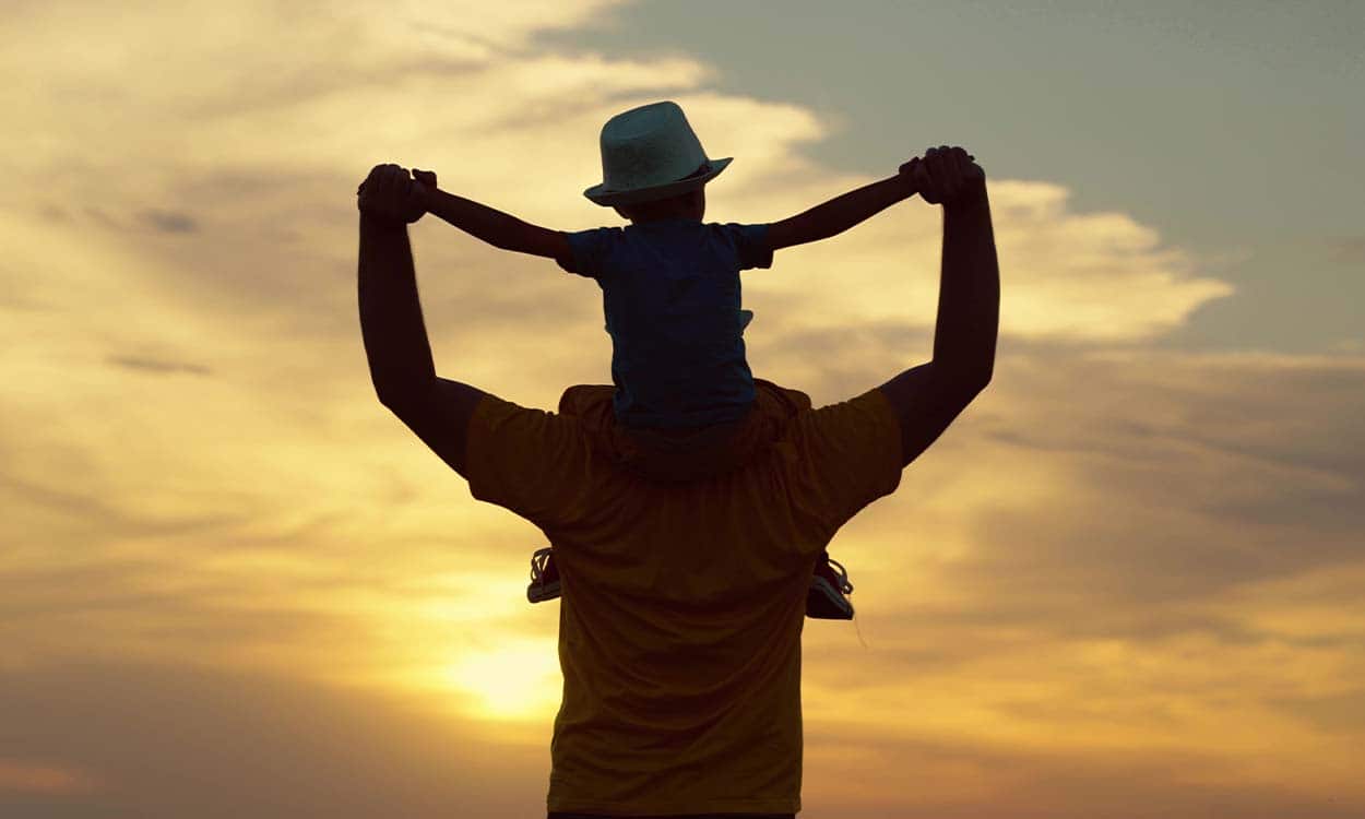 pai carrega o filho pelas costas no por do sol