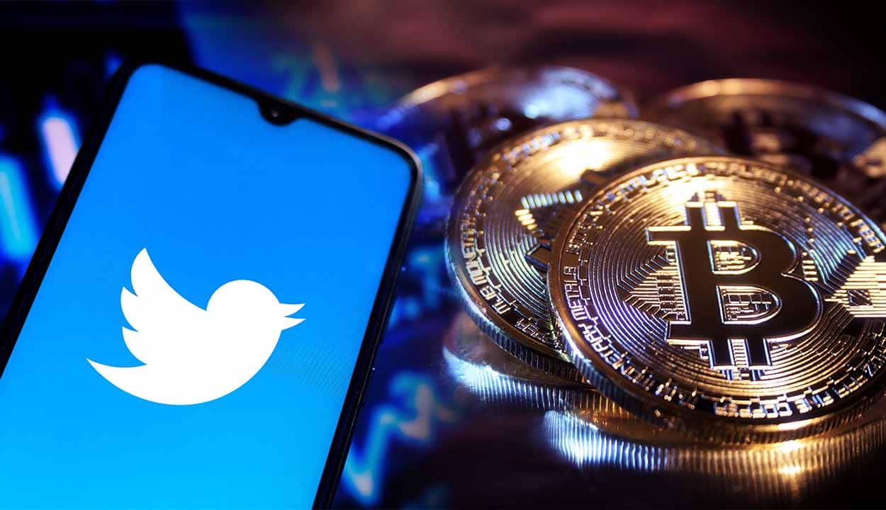 Celular com aplicativo do Twitter aberto e criptomoedas de Bitcoin ao lado
