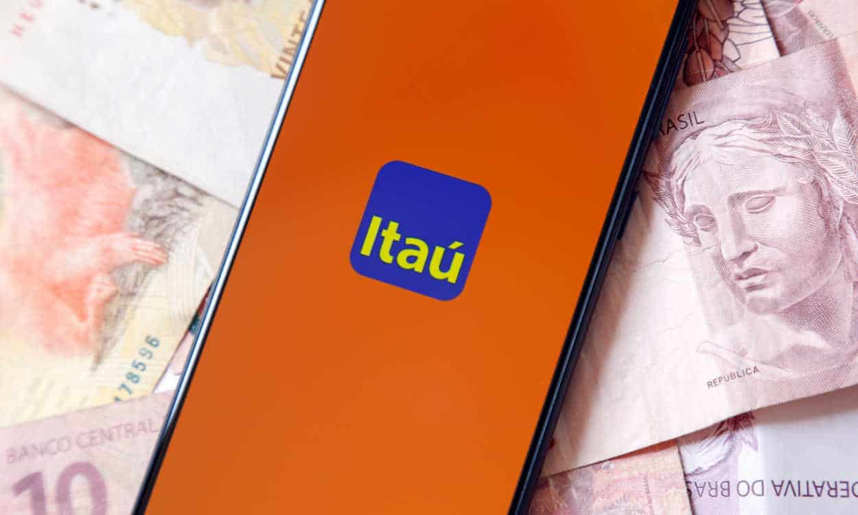 Celular com a logo do Itaú na tela em cima de várias notas de real