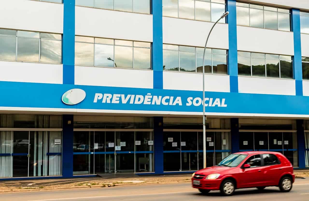 Fachada de agência do INSS com um carro vermelho na frente.
