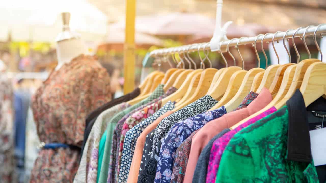 imagem de uma arara de peças em um brechó de roupas, ao lado tem um manequim com um vestido