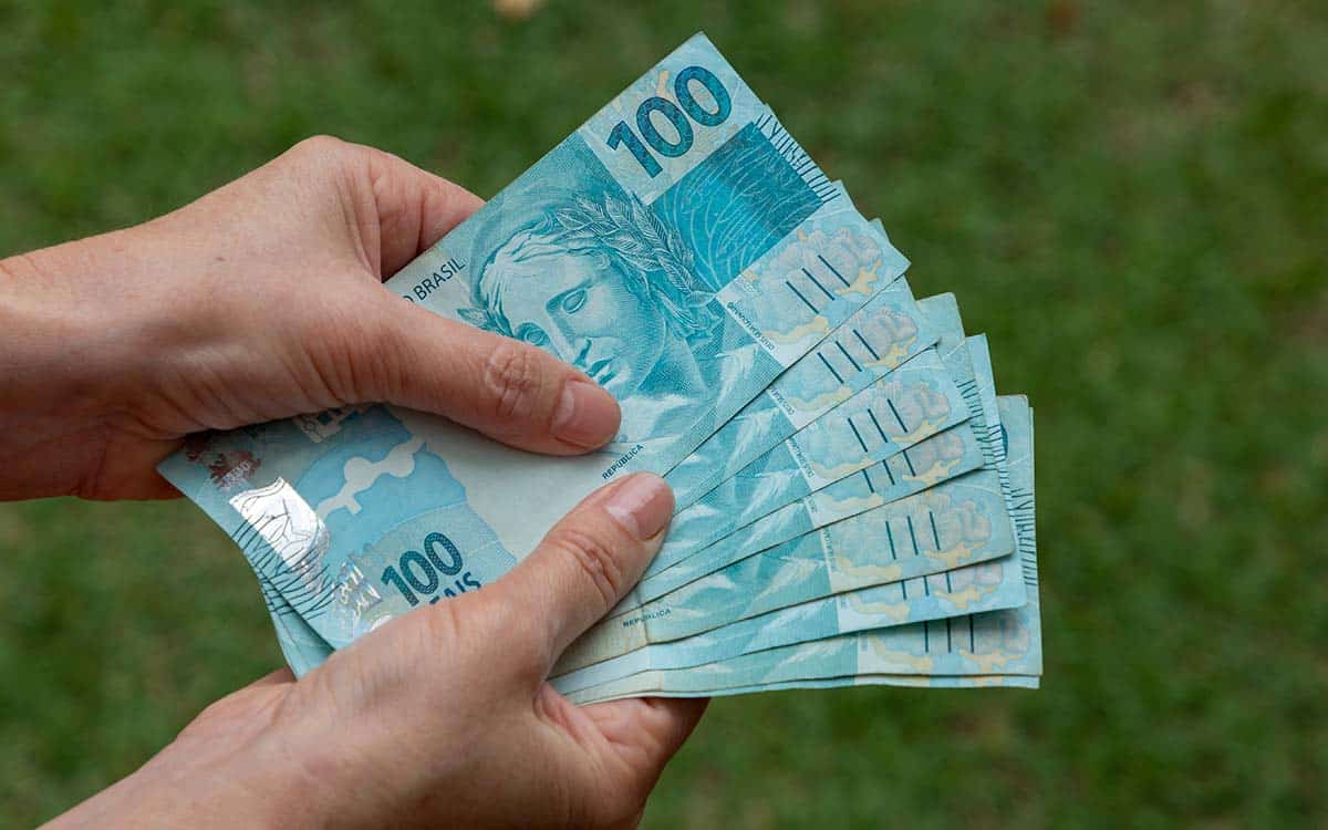 Mãos segurando diversas notas de 100 reais
