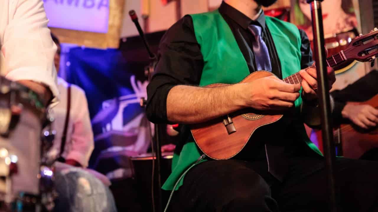 imagem de um cantor de pagode tocando viola com uma banda num bar