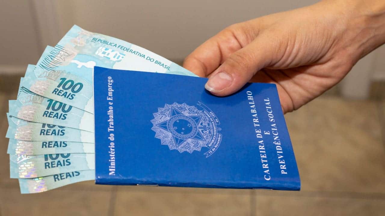 pessoa segurando uma Carteira de Trabalho e Previdência Social com notas de 100 reais dentro