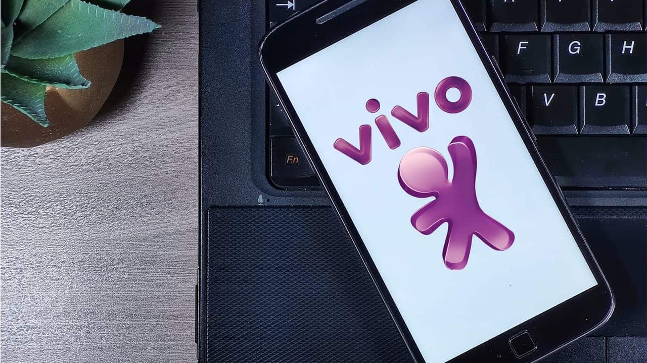 Tela de celular com logo da operadora Vivo. Ao fundo, teclado de um notebook.
