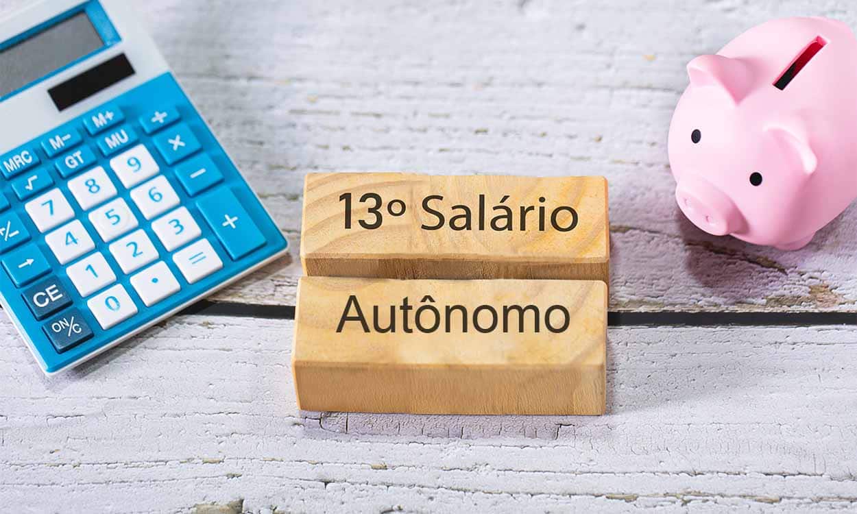 Papéis em cima de uma mesa sobrepostos por uma calculadora, um cofre de porquinho e dois bloquinhos de madeira com os dizeres "13º salário autônomo"