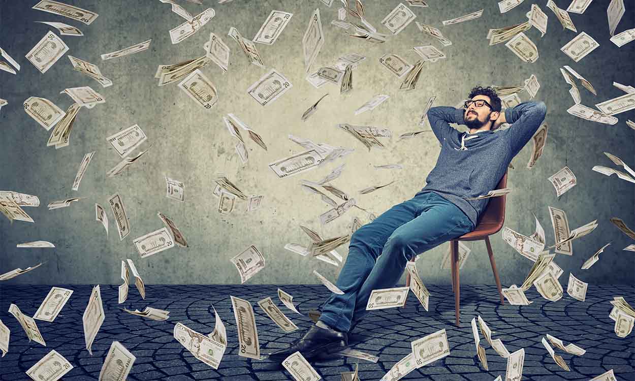 Homem sentado, com dinheiro voando ao redor dele. liberdade financeira