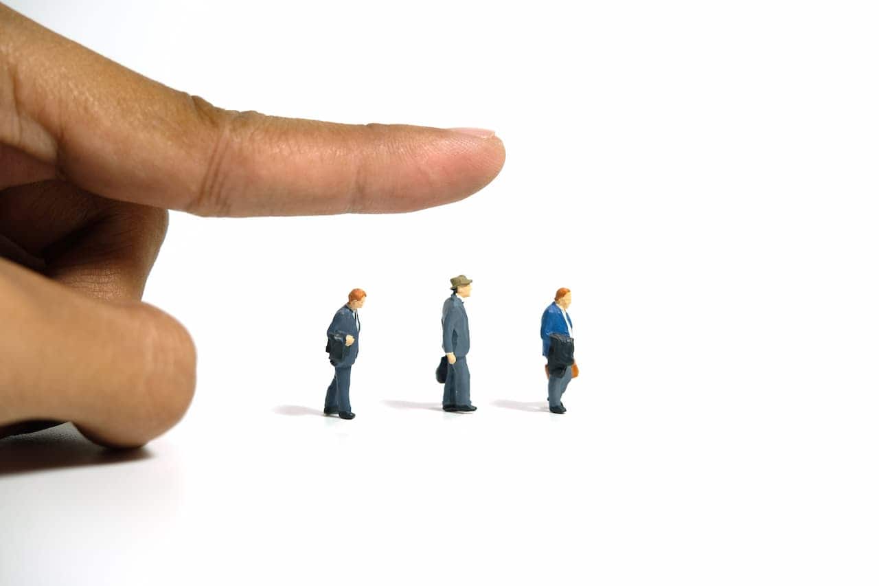 dedo apontando direção que bonecos em miniatura representando funcionários demitidos estão seguindo