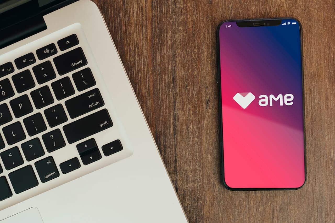 Ao lado de teclado de um laptop, celular exibe logo da Ame Digital