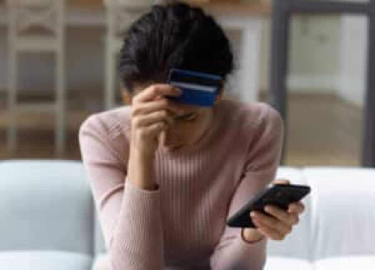 mulher cabisbaixa com cartão em uma mão e celular em outra golpe financeiro